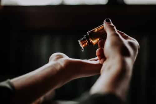 A person's hand holding an essential oil bottle used for natural pest control.